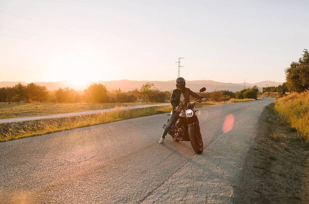 Motorcyclist riding on a quiet road at sunset, emphasizing safe and gentle riding.