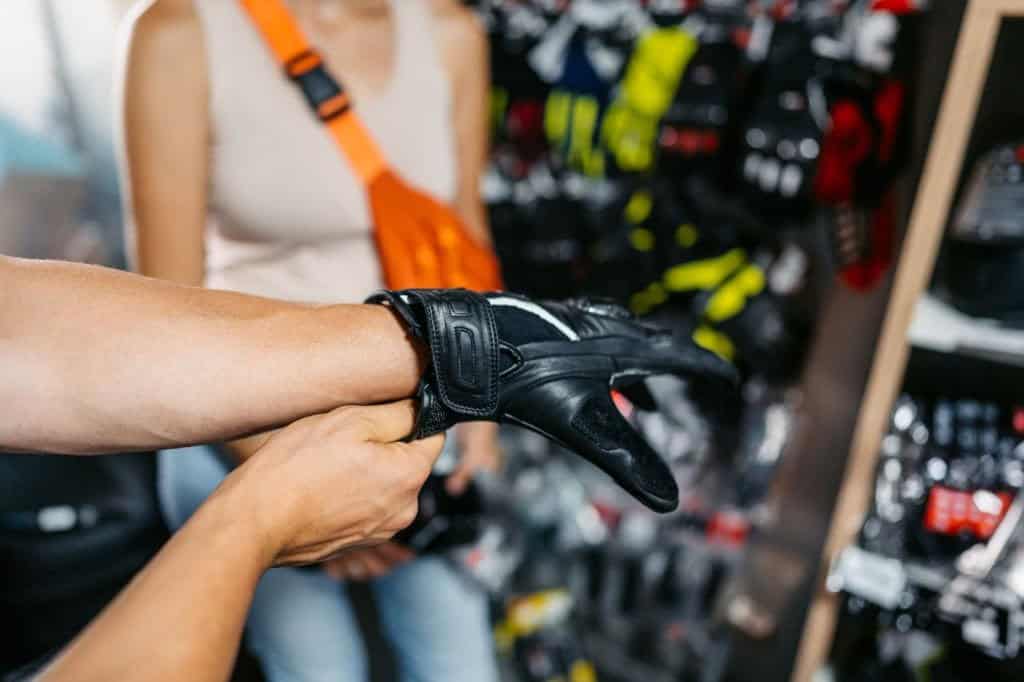 Person trying on leather motorcycle gloves inside a gear shop, checking fit and closure