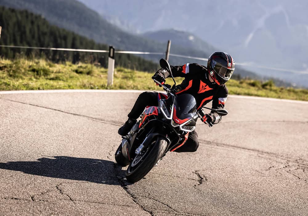 Motorcyclist leaning into a curve on a sportbike, wearing full Dainese gear on a scenic mountain road