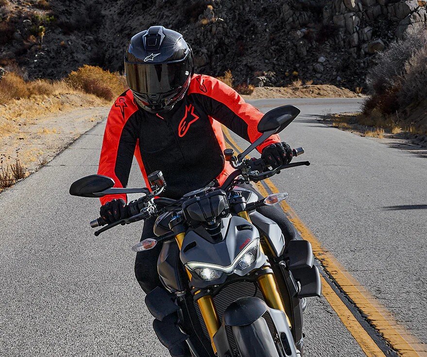 Motorcyclist wearing an Alpinestars jacket with Tech-Air 5 Plasma system on a twisty road, illustrating under-jacket airbag use.