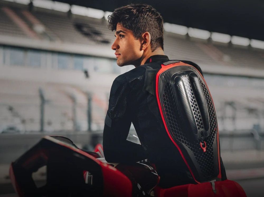 Motorcyclist sitting on a sportbike at a racetrack, wearing a modern motorcycle airbag vest with visible back protection.