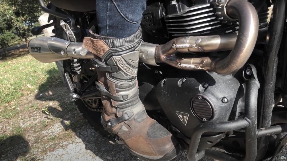 Close-up of Forma Adventure Boots on footpeg of a Triumph motorcycle in sunlight