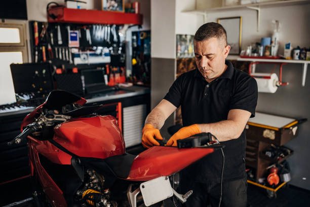 Man working on a red sport motorcycle in a garage, connecting or checking a battery charger under the seat.