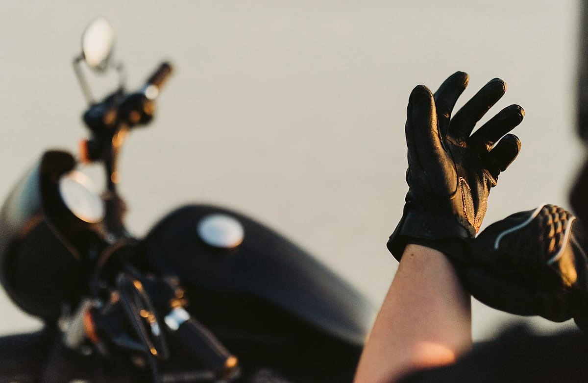Motorcyclist putting on leather gloves near a parked motorcycle
