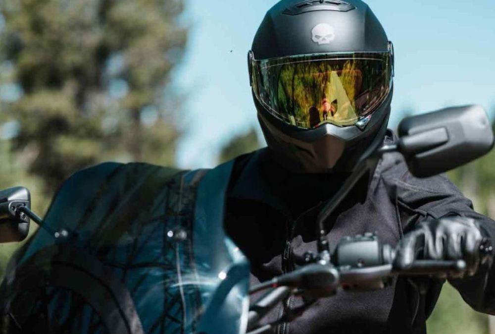 Rider wearing a matte black full-face helmet with skull logo and reflective visor on a cruiser motorcycle