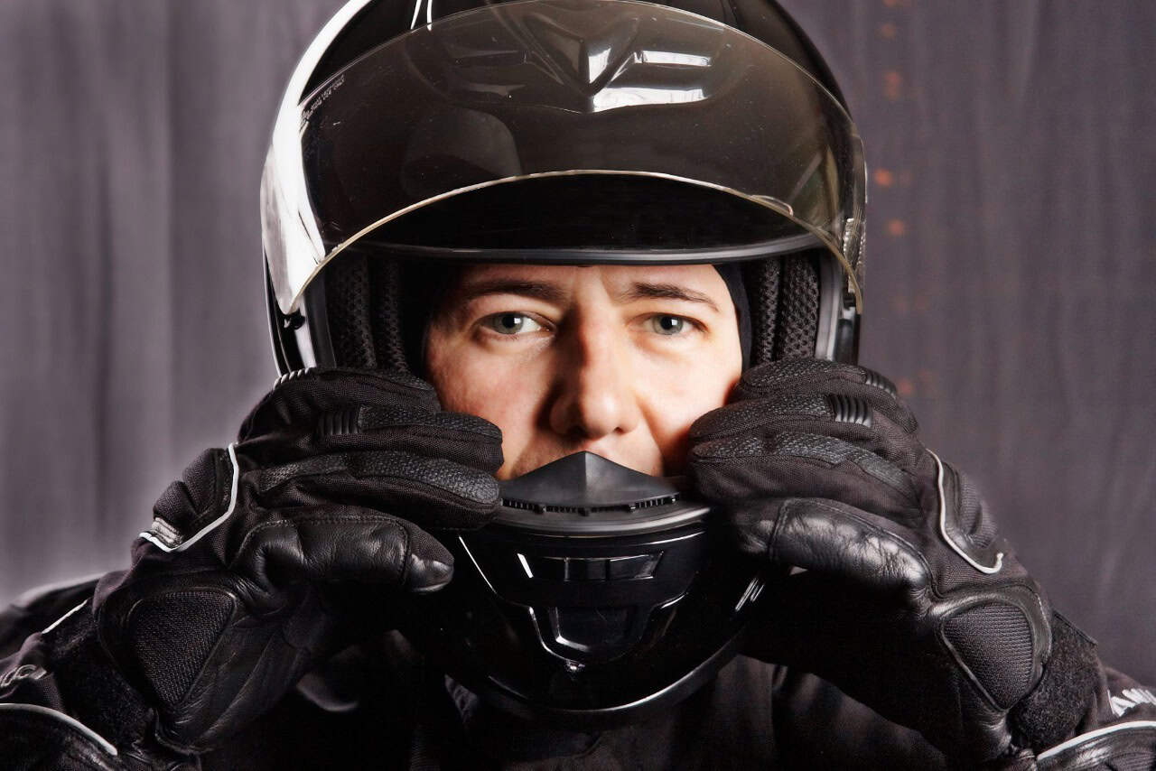 Close-up of rider adjusting a full-face motorcycle helmet with gloved hands.