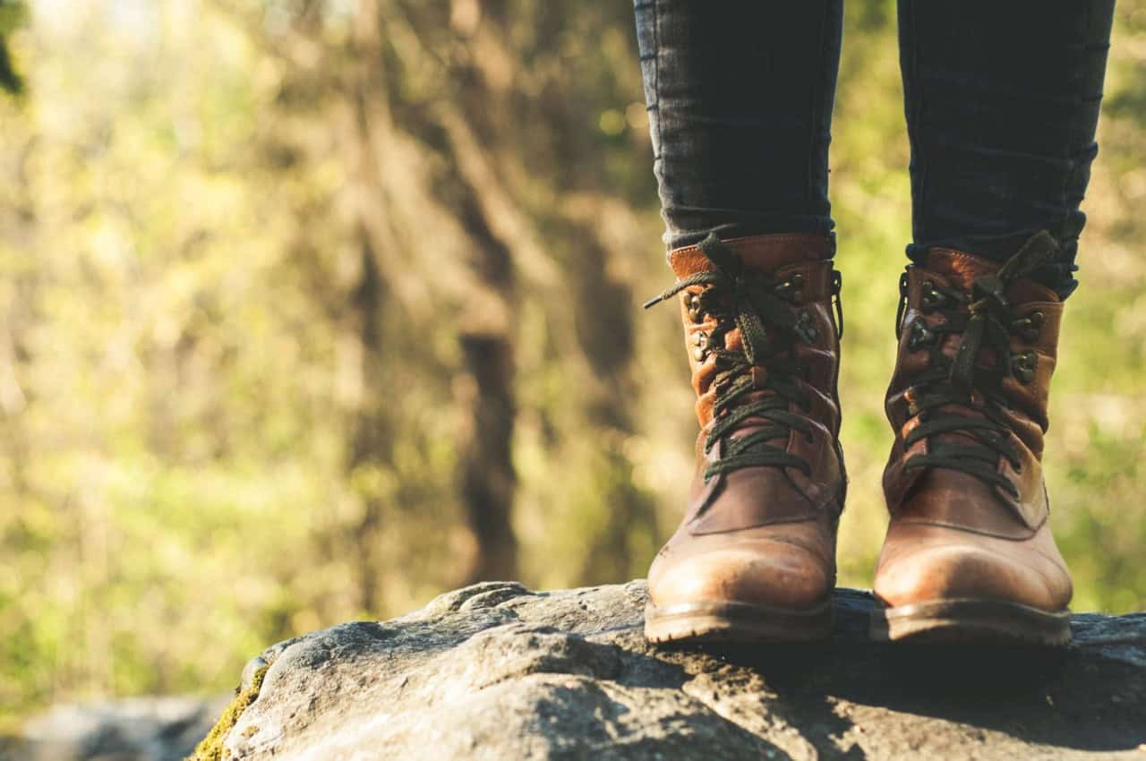 Close-up of worn hiking boots standing on a rock in a forested area