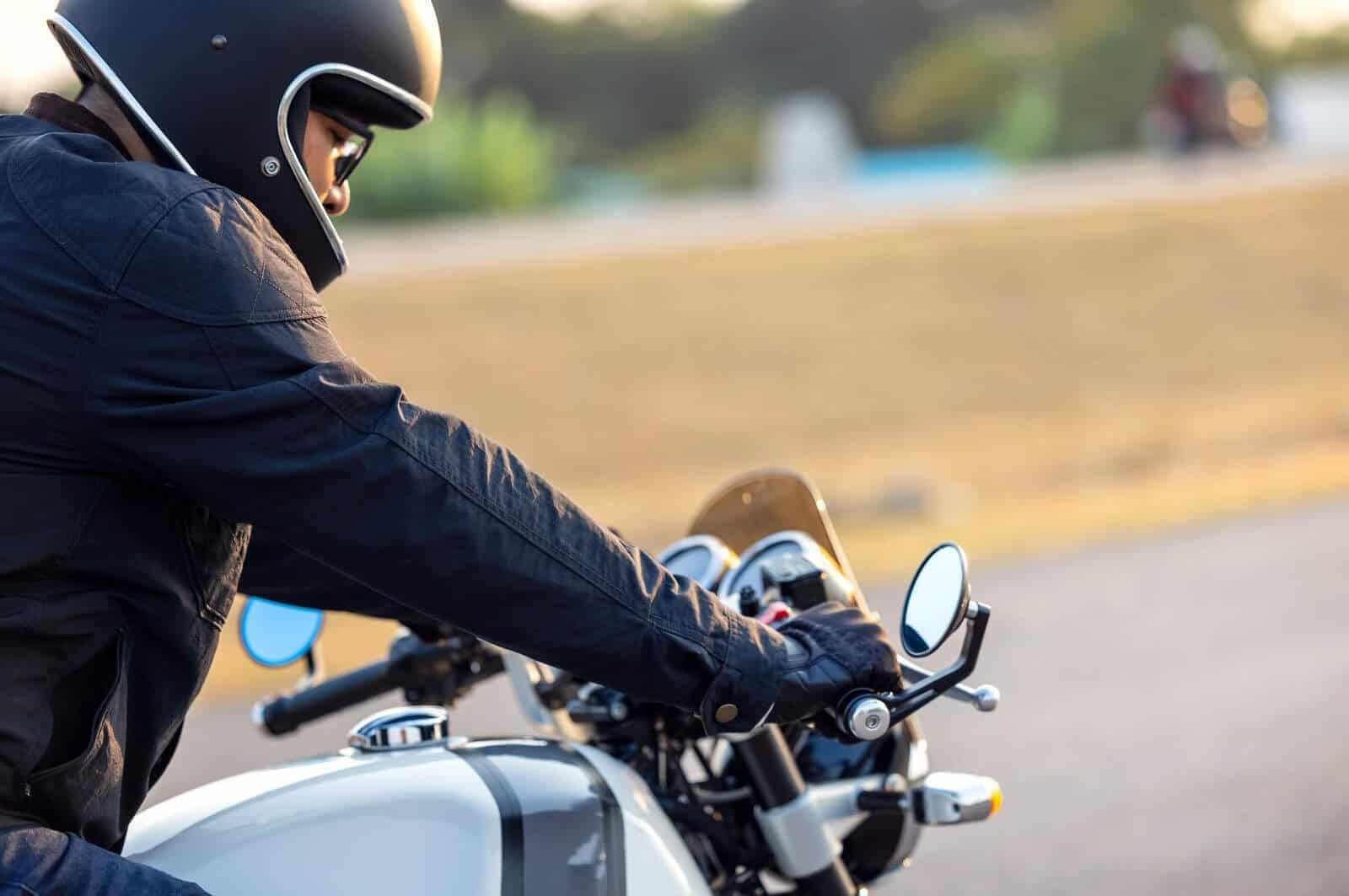 Rider wearing vintage-style gloves and helmet on a café racer motorcycle