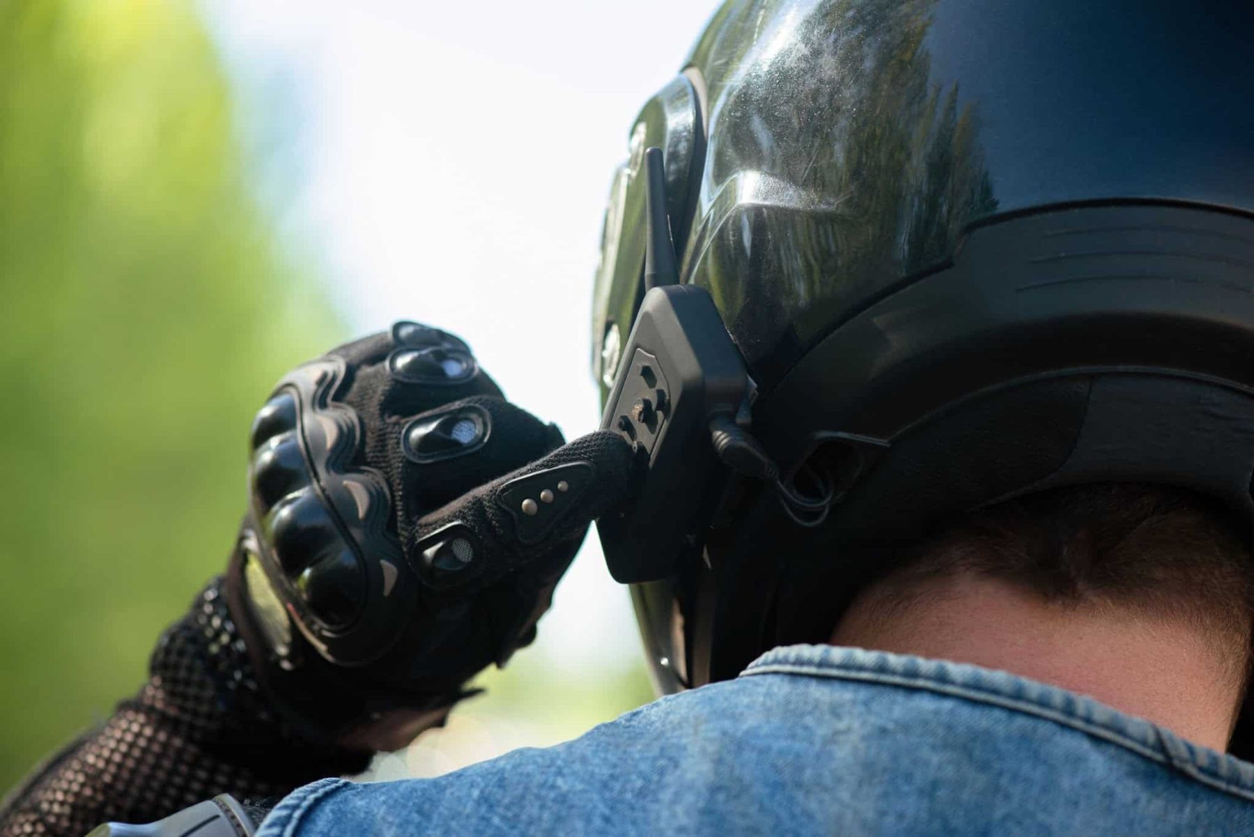 Close-up of a motorcyclist adjusting their Bluetooth headset mounted on a helmet, illustrating frustration with poor audio devices.