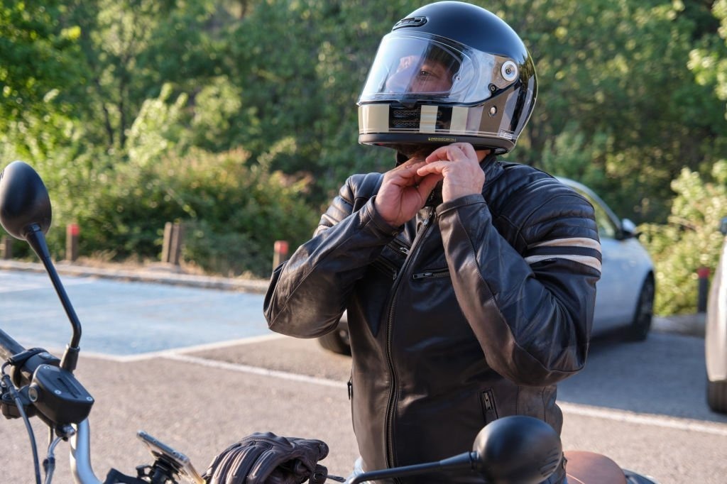 Motorcyclist securing helmet with visible forehead pressure point risk