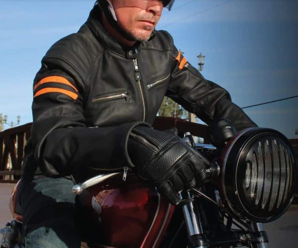 Rider wearing Joe Rocket Cafe Racer gloves and vintage-style gear, gripping the handlebars of a custom motorcycle.