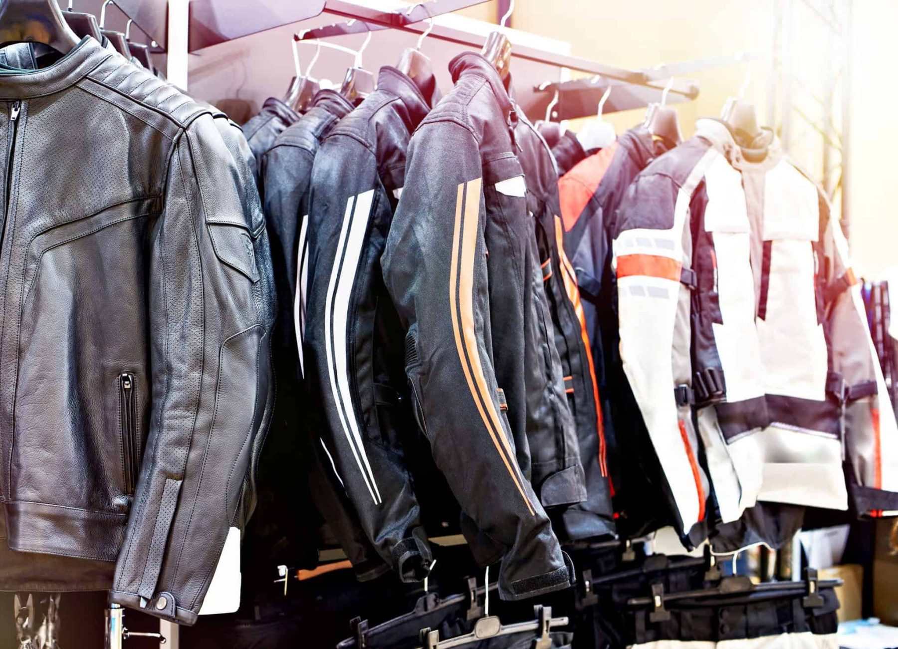 Motorcycle jackets of various styles and materials hanging on a display rack in a gear store