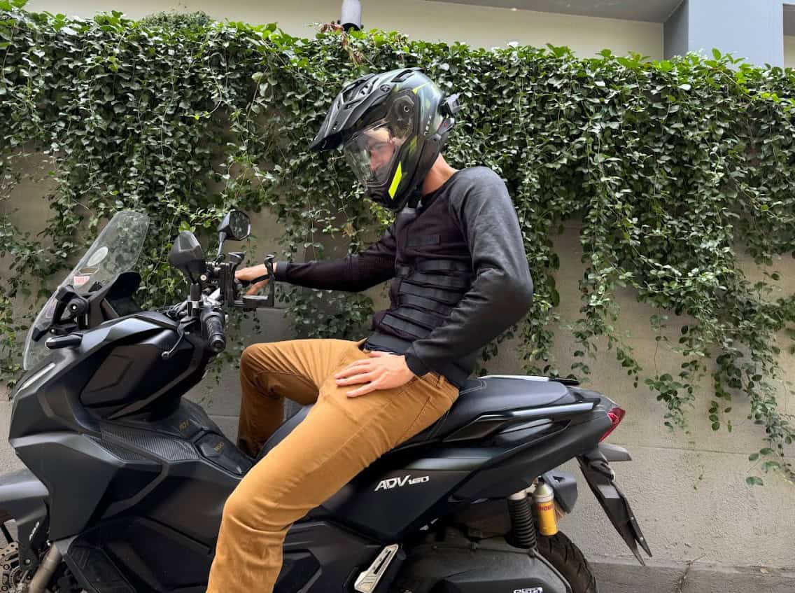 Motorcyclist in a ventilated summer jacket and helmet seated on a scooter in urban heat, ready to ride