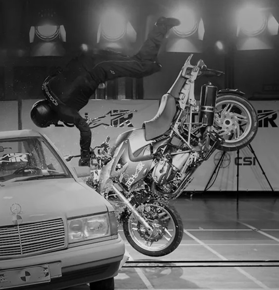 Crash test showing a motorcyclist being thrown over a car during a collision, demonstrating impact in a controlled environment.