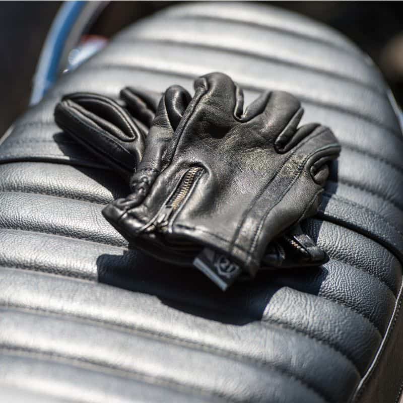 Highway 21 Recoil leather motorcycle gloves with vintage zipper closure, resting on a black ribbed seat.