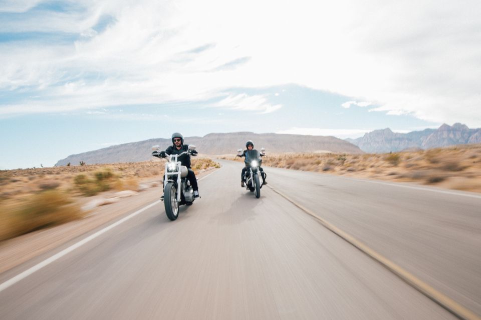 Two motorcyclists riding on an open road through a dry desert landscape under a cloudy sky.