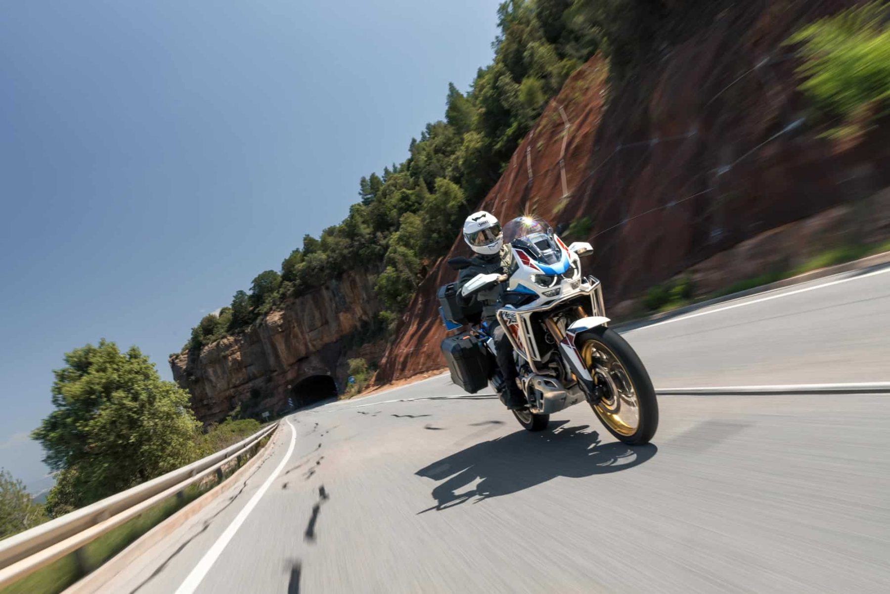Motorcyclist riding at speed through a mountain curve in full summer gear and helmet under clear blue skies