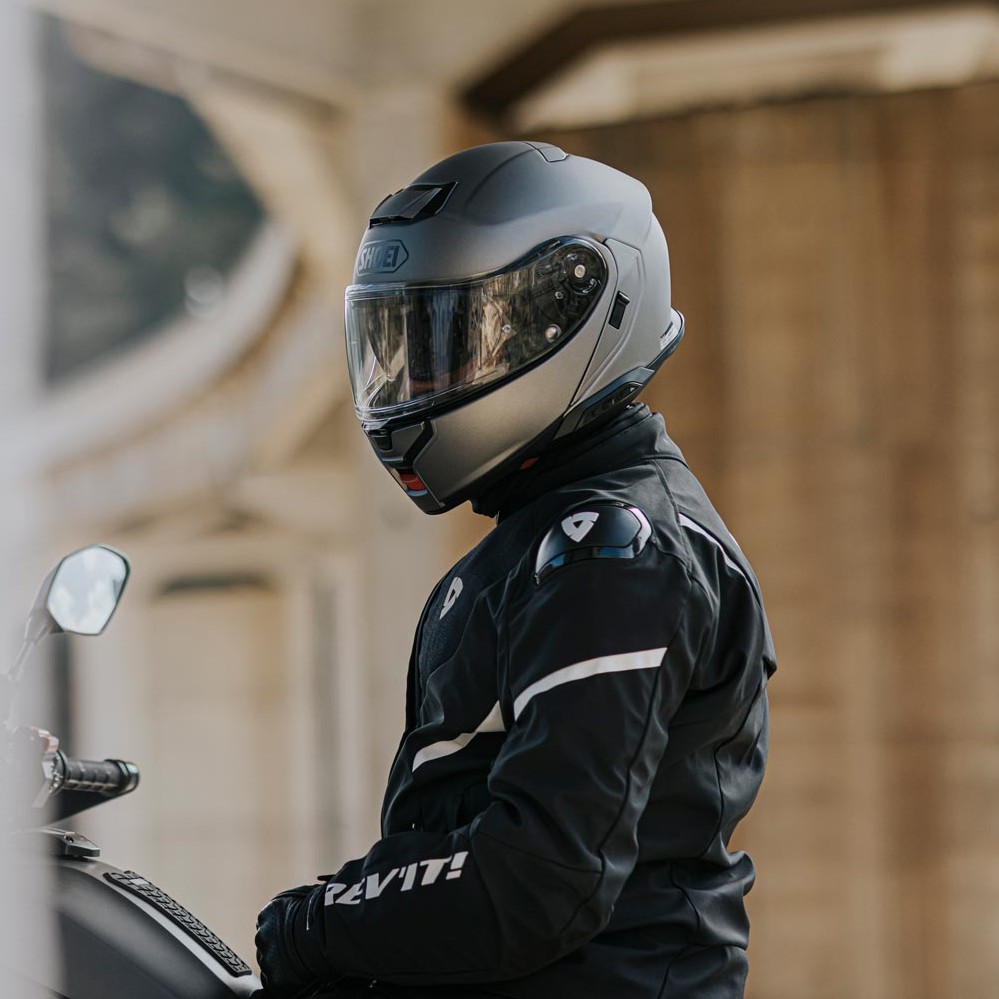 Motorcyclist wearing a Shoei modular helmet and REV’IT! jacket, ready to ride