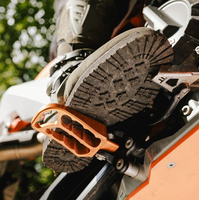Close-up of a lugged adventure boot sole on a dirt bike footpeg, showing tread pattern and functional grip.