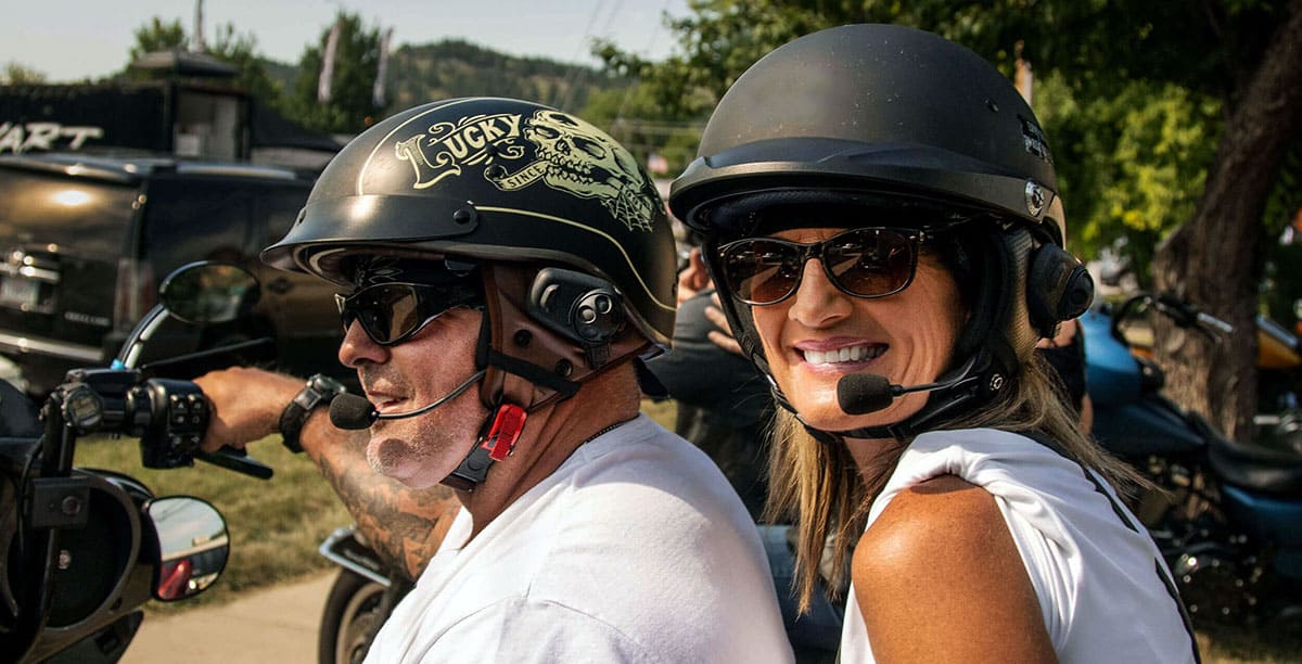 Two riders on a cruiser motorcycle wearing half helmets with Sena SPH10H-FM Bluetooth headsets and boom mics
