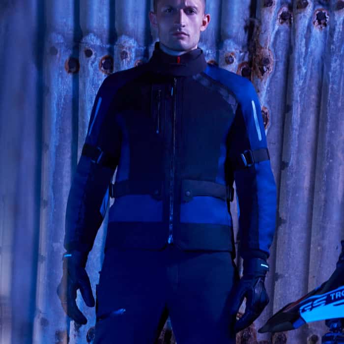Motorcyclist wearing a Spidi touring jacket in a dramatic urban setting with blue lighting