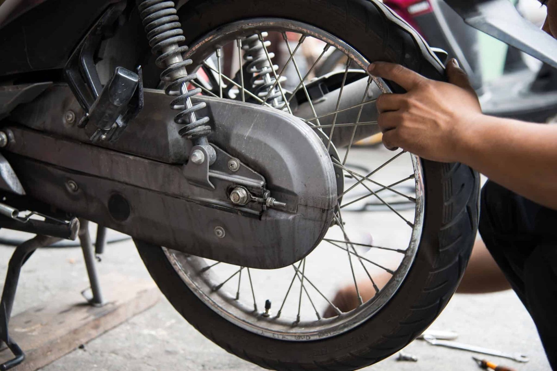 Motorcycle mechanic checking rear tire alignment and condition on a center stand