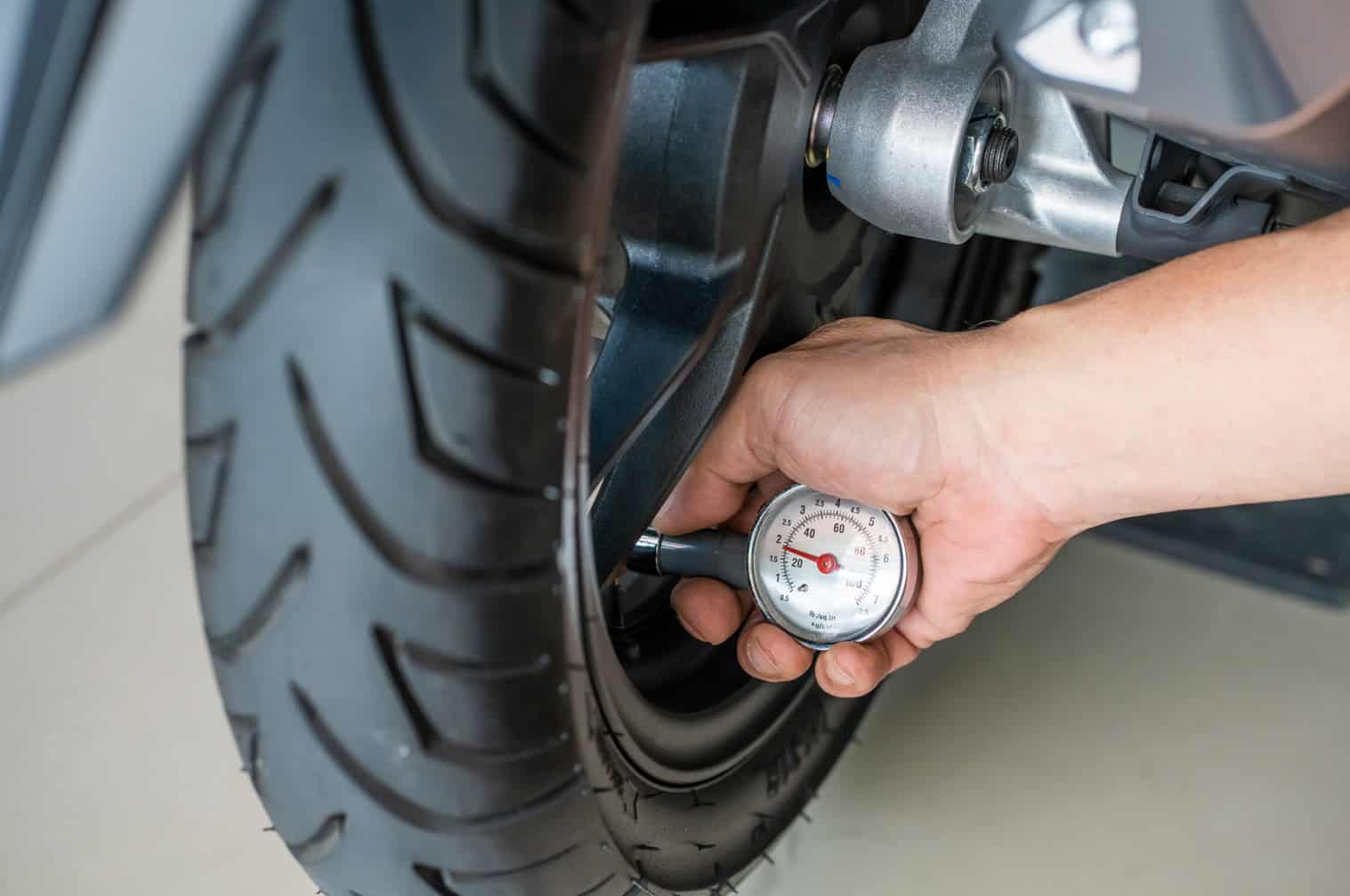 Hand using a tire pressure gauge on a motorcycle tire to check air pressure
