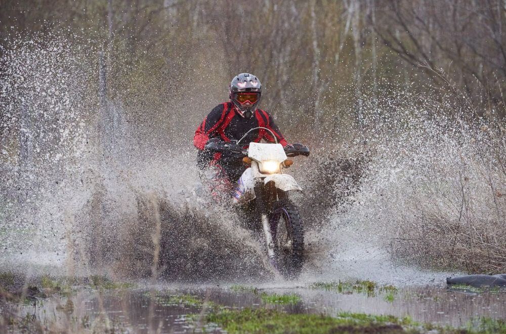 Rider splashing through a waterlogged trail on a dual-sport motorcycle, demonstrating waterproof gear performance.