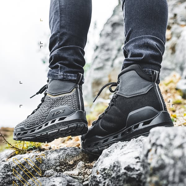 Close-up of TCX Climatrek Surround waterproof motorcycle boots on rocky terrain, worn with jeans, showcasing rugged outdoor capability.