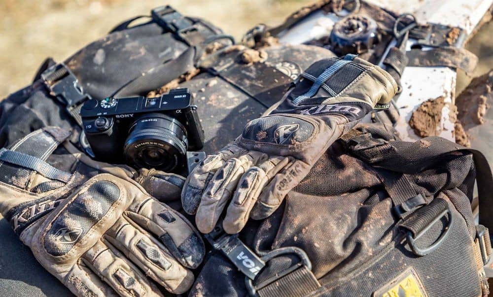 Dirty motorcycle gloves resting on gear after an off-road ride, showing the need for post-ride cleaning and care.