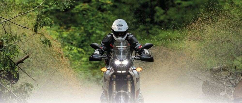 Adventure rider splashing through forest trail in Arai Tour-X5 helmet, showcasing its off-road and on-road adaptability