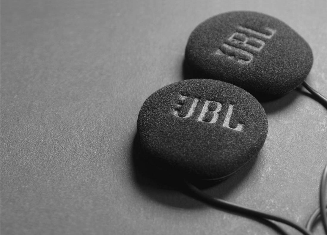 Close-up of Cardo 45 mm JBL helmet speakers with black foam covers and visible JBL branding, lying on a flat surface.
