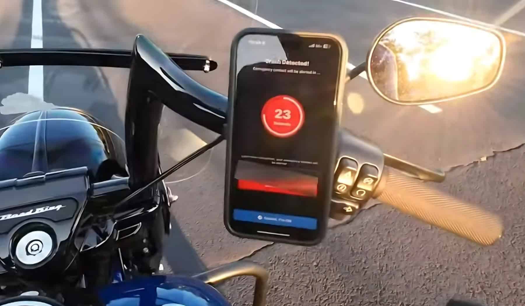 Smartphone mounted on motorcycle handlebar showing crash detection countdown screen with emergency alert feature active.