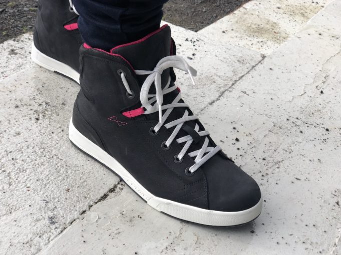 Close-up of Forma Swift Dry Women’s waterproof motorcycle shoes with white soles and pink accents, worn by a rider on concrete steps.