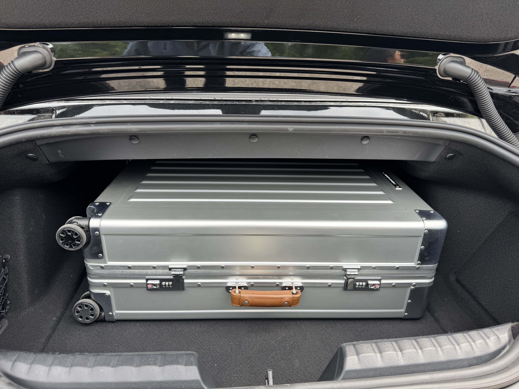 Sterling Pacific 90L suitcase neatly packed in the trunk of a sports car, showcasing its size, rugged build, and sleek aluminum finish.