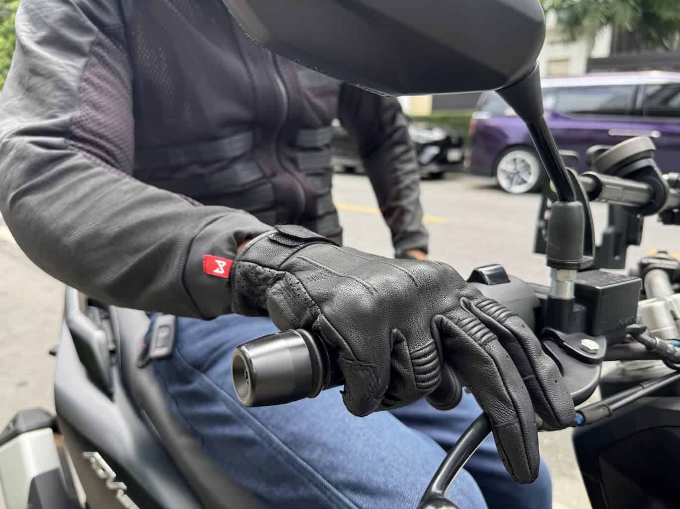 Rider wearing Ivy gloves on motorcycle throttle, urban backdrop