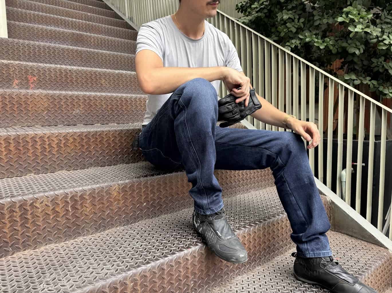 Rider in Pando Moto Arnie Slim jeans sitting on metal stairs, holding motorcycle gloves