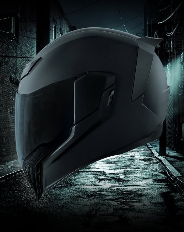 Icon Airflite Dark Rubatone helmet with matte black finish and oversized visor, shown in a moody urban alley for a Gotham-style vibe.