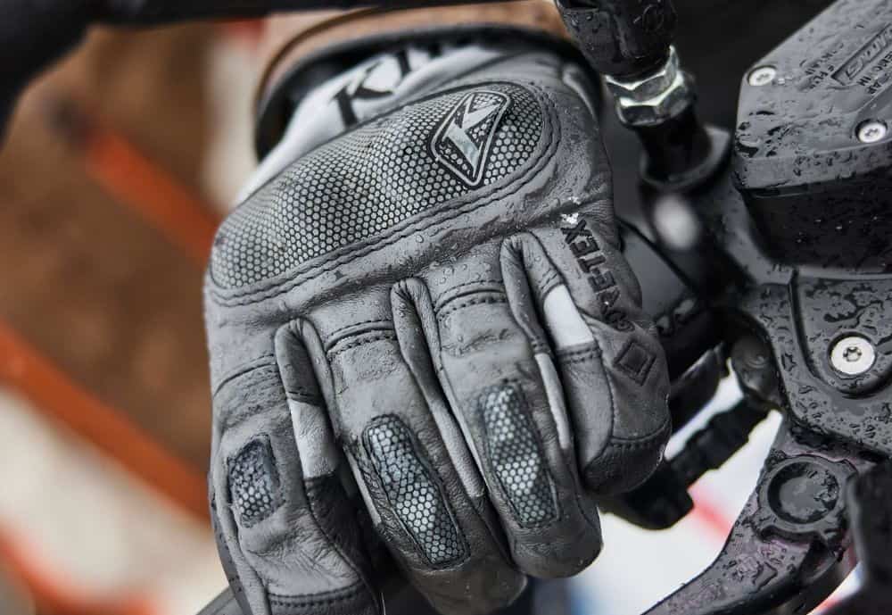 Close-up of waterproof Klim motorcycle glove gripping a wet handlebar