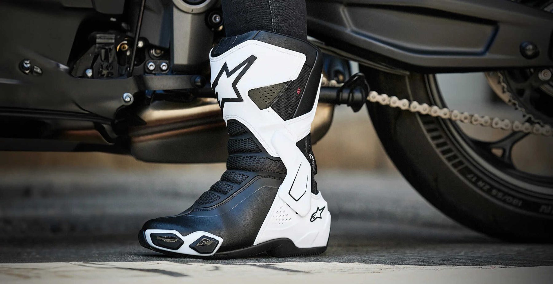 Alpinestars Stella SMX-6 V3 Drystar women’s sport motorcycle boots in black and white, worn on a bike with close-up view of footpeg area.