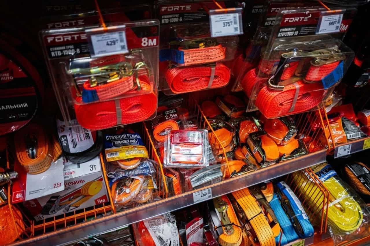 Wall display of various tie-down and ratchet straps in a hardware store, showing different lengths and hook types