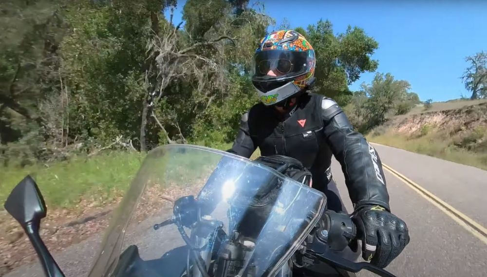 Motorcyclist riding through a scenic road in full gear, wearing a graphic helmet and black leather jacket, visor down.