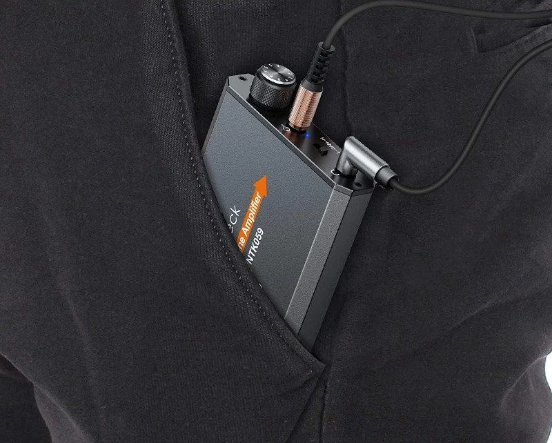 A compact Neoteck headphone amplifier connected to an audio cable and tucked into a hoodie pocket