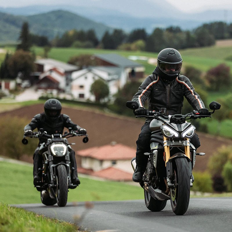 Two motorcyclists riding through countryside wearing full-face helmets with Bluetooth comms