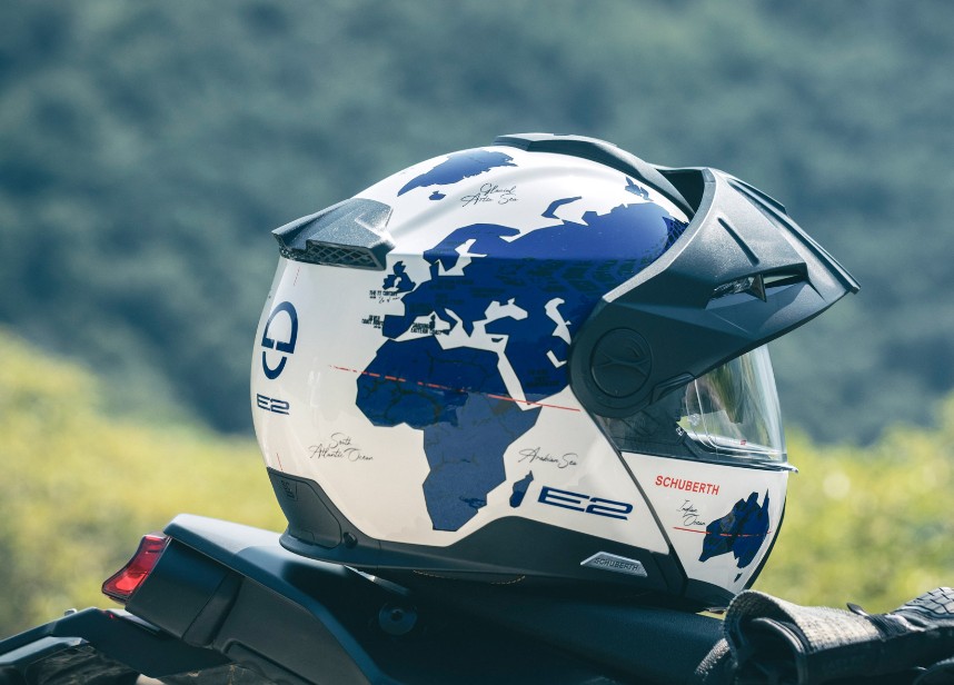 Schuberth E2 ADV modular helmet with world map graphic resting on motorcycle