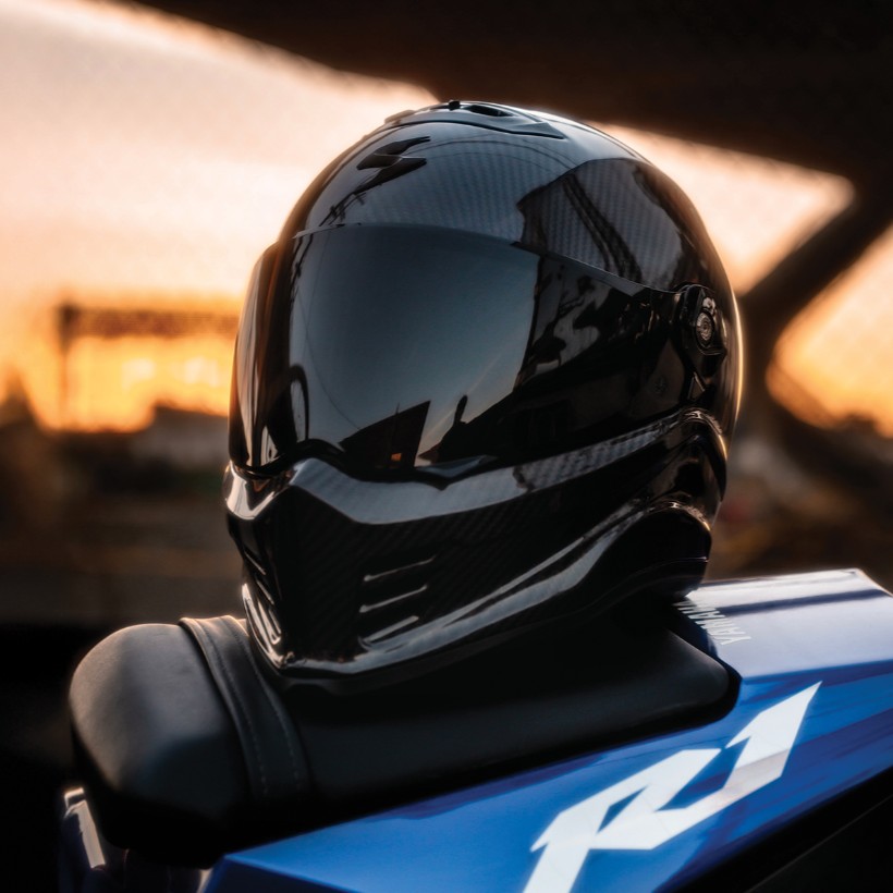 Scorpion EXO Covert FX Carbon motorcycle helmet with a matte carbon finish and tinted visor, placed on a sportbike seat at sunset.