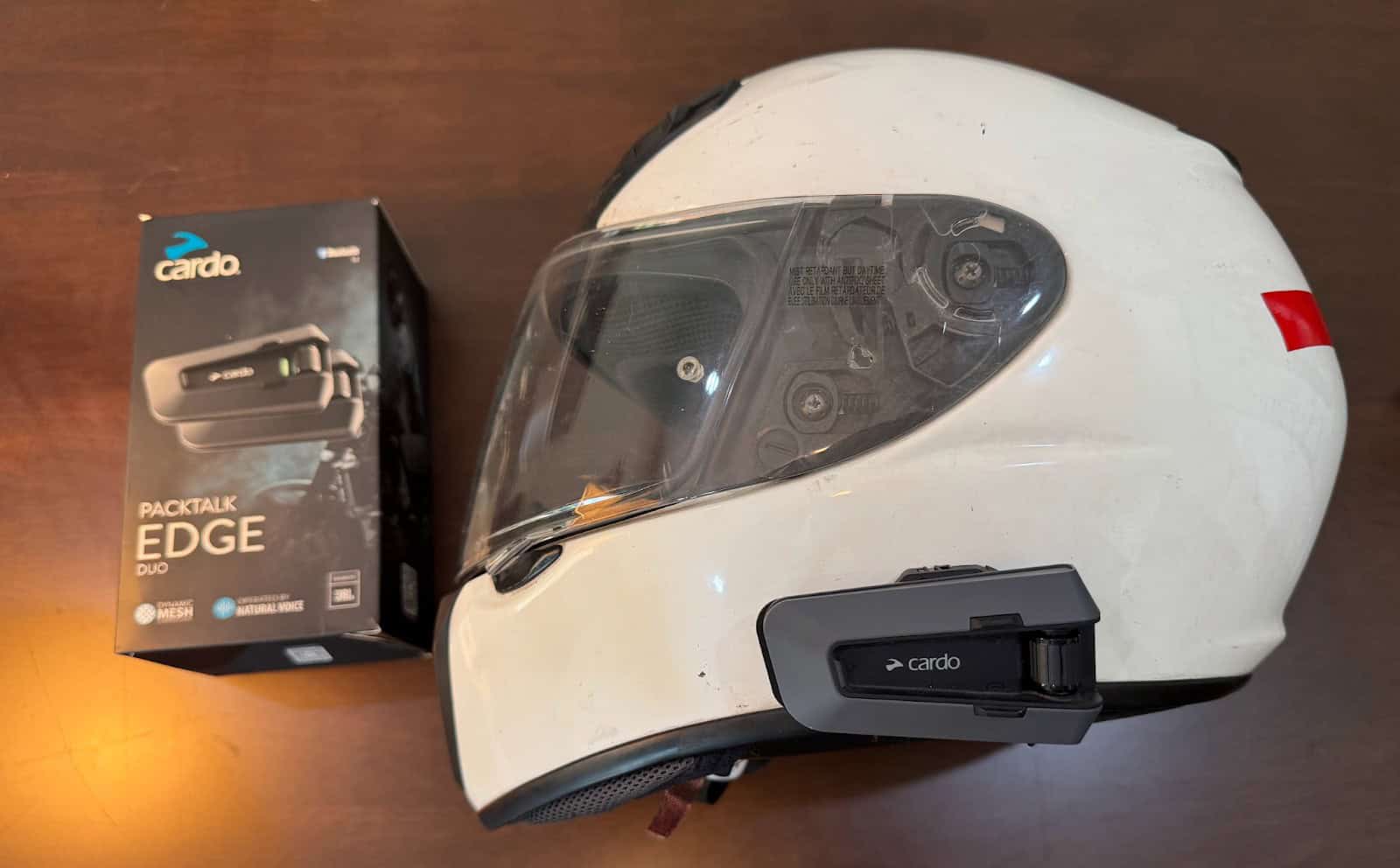 Cardo Packtalk Edge installed on a white full-face helmet next to original product box