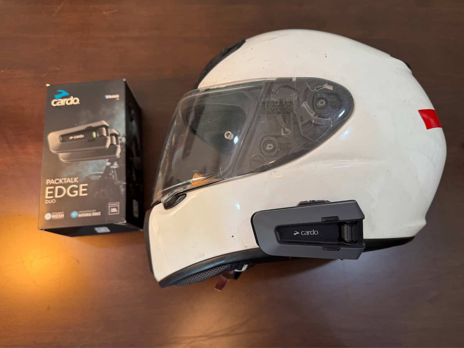 Cardo Packtalk Edge mounted on a white motorcycle helmet beside product box
