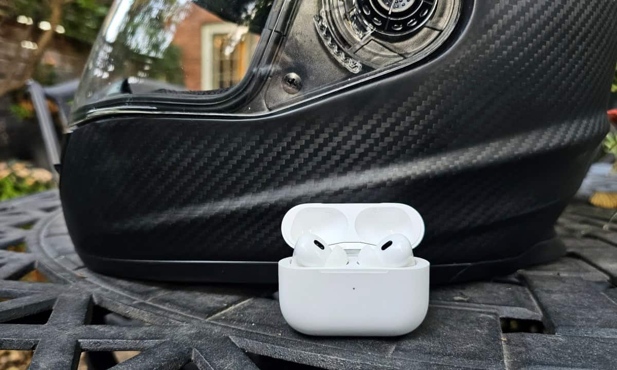 Apple AirPods Pro 2 in front of a carbon fiber motorcycle helmet on a table
