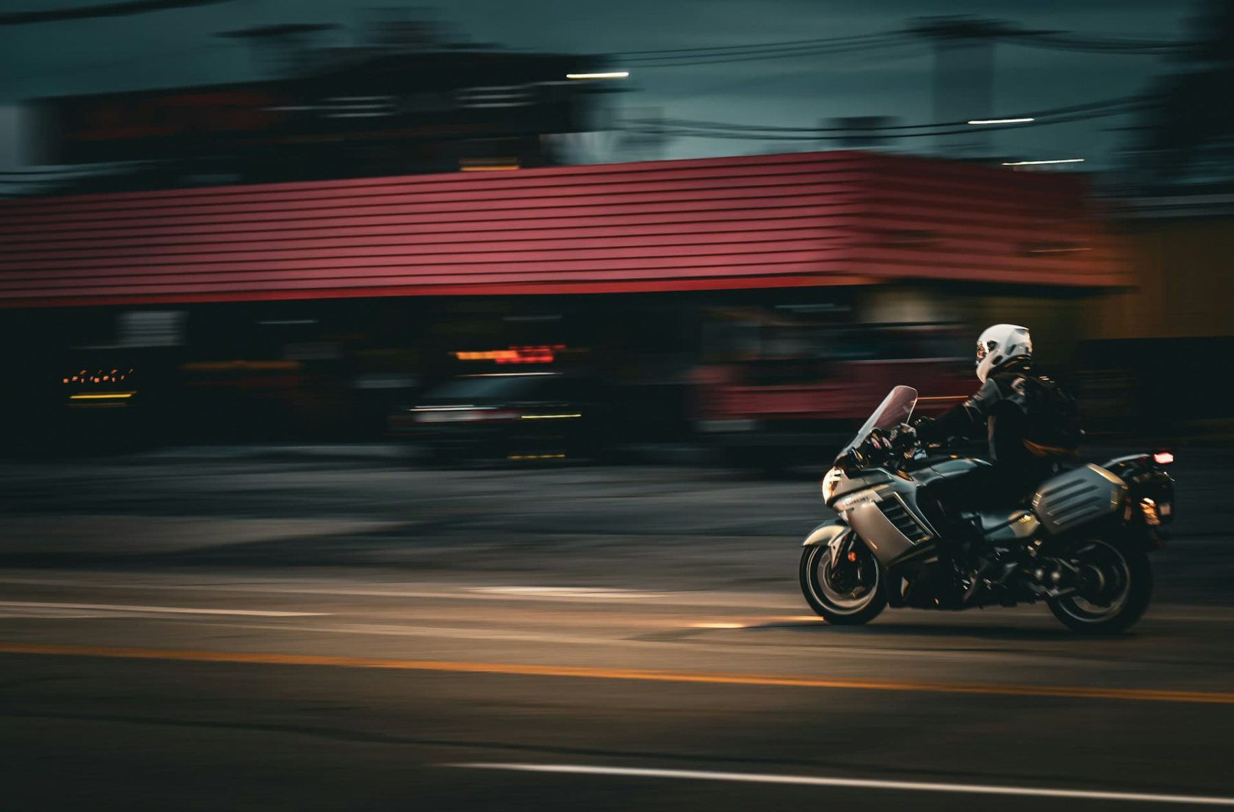 Motorcyclist riding at speed through a city at night, with motion blur emphasizing wind and movement.
